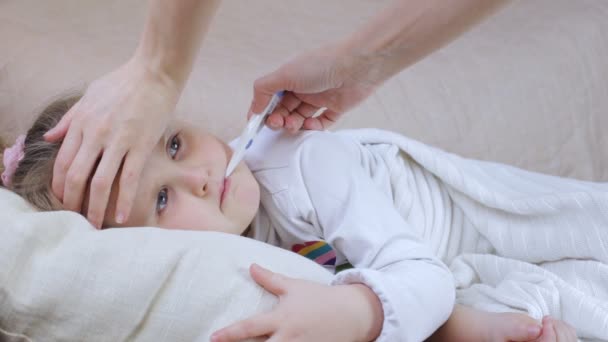 Sick girl with a thermometer. Mother touch her head - Video