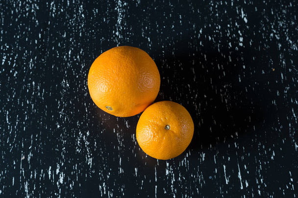 Twee hele sinaasappelen op zwarte houten keukentafel. - Foto, afbeelding