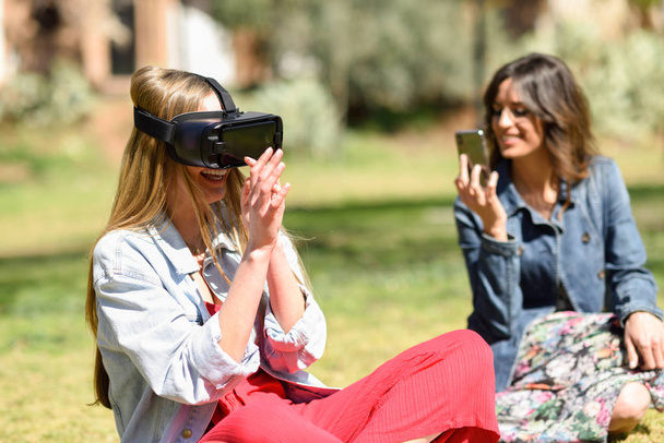 Mulher olhando em óculos VR e gesticulando com as mãos ao ar livre
 - Foto, Imagem