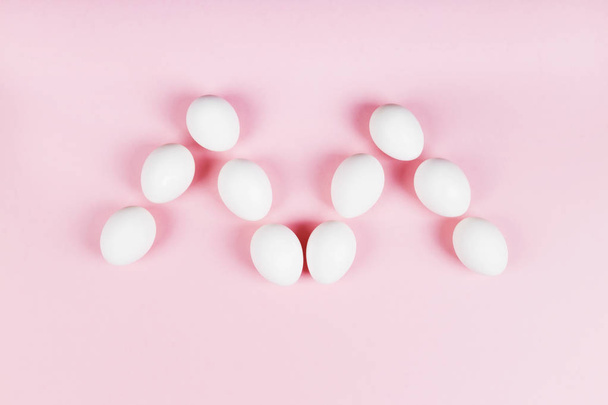 White eggs in form of letter "m" on pink background. Concept gen - Φωτογραφία, εικόνα