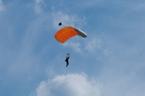 Парашютист с оранжевым парашютом против чистого голубого неба
 - Фото, изображение