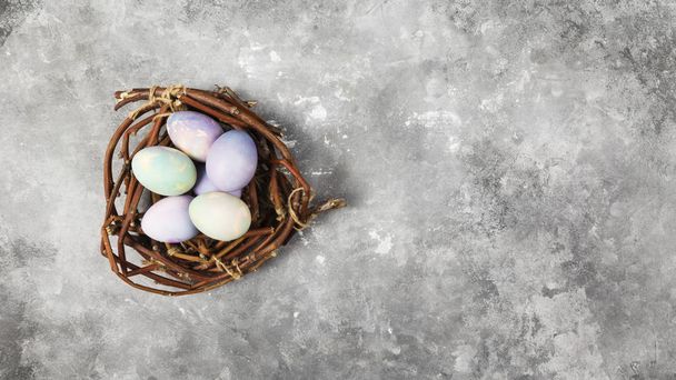 Multicolored eggs for Easter in nest on gray background. Top vie - Foto, Imagen