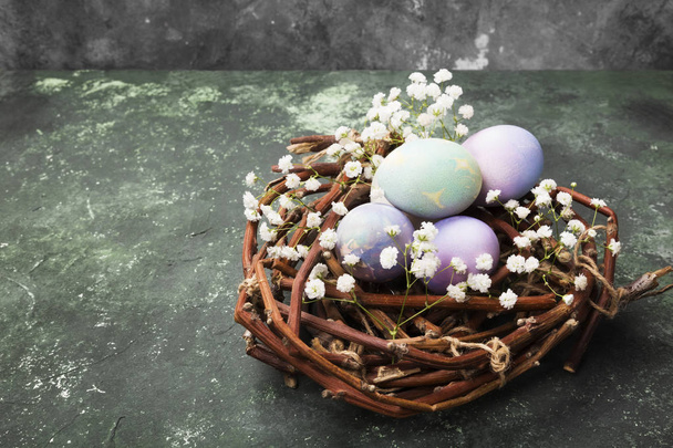 Multicolored eggs for Easter in nest with flowers on green backg - Φωτογραφία, εικόνα