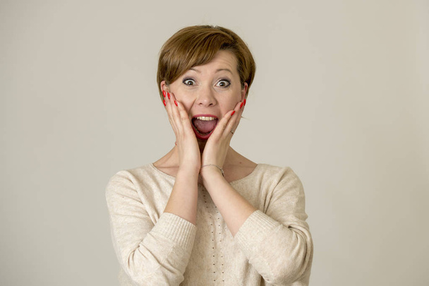 young happy and surprised red hair woman looking to camera delighted astonished and in surprise face expression isolated on grey background - Photo, image