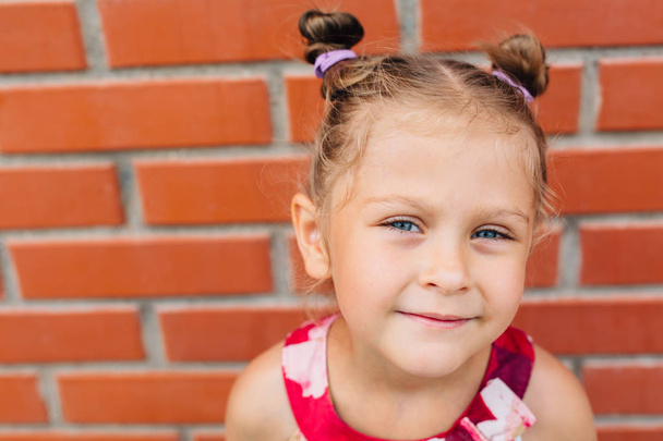 Cute little cheerful girl in dress standing near brick wall. - Fotoğraf, Görsel