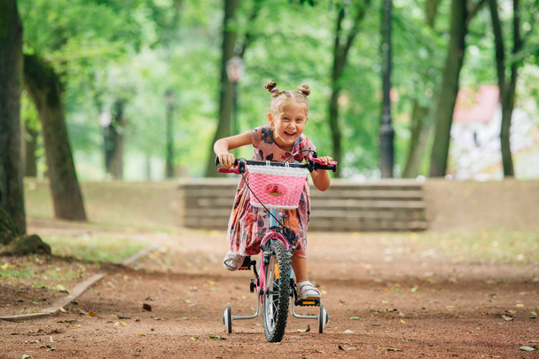 Smiling little girl on a bicycle in park. Cheerful child riding - Foto, immagini
