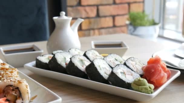 Kaksi sarjaa sushia rullaa tyylikkäässä, kauniisti sisustetussa kahvilassa. Ravintola Japanilainen keittiö pöydällä vieressä sushi posliini teekannu soijakastike ja lautanen
 - Materiaali, video