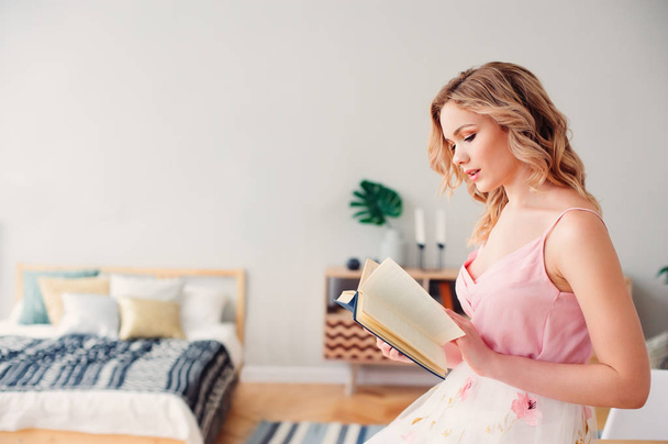 young beautiful woman reading book at home in cozy weekend morning, wearing trendy spring skirt and top. - Zdjęcie, obraz