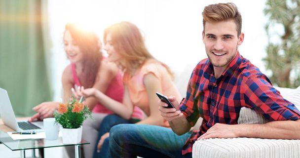 modern guy with a smartphone and his friends sitting on the couch - Photo, Image
