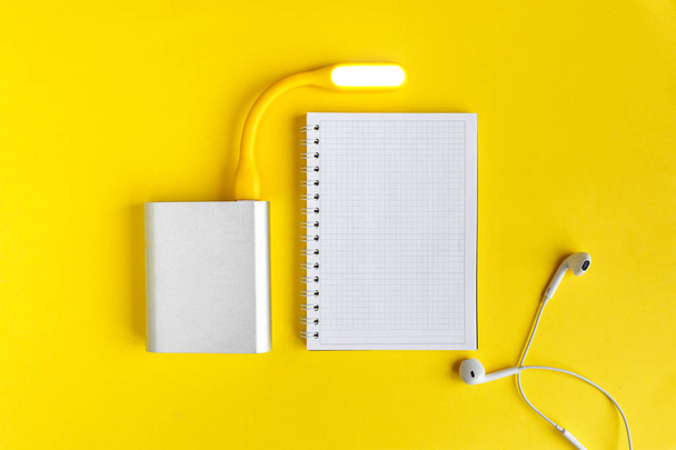 Notebook on office table with power bank and mini lamp. Top view desk, flat lay yellow color background concept. - Photo, image