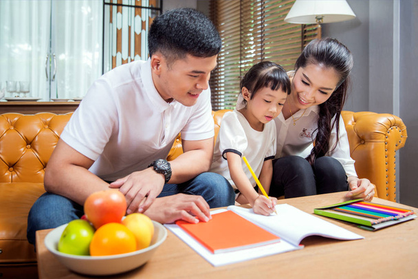 Padre, madre e figlia asiatici che lavorano a casa insieme in soggiorno, questo immage può utilizzare per l'istruzione, la casa e il concetto di famiglia.
 - Foto, immagini