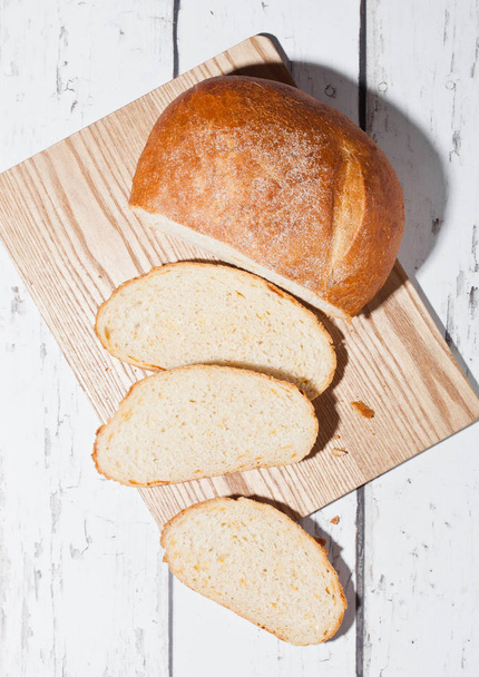Freshly baked bread loaf with pieces on wood board - Foto, afbeelding