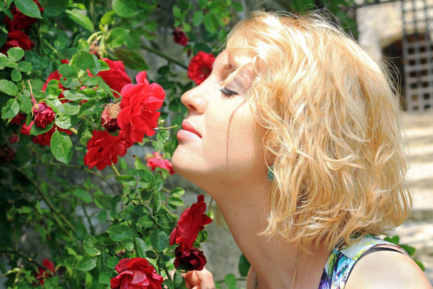 Genç ve güzel bir kadın kırmızı bir gül kokuyor. Gül kokusu - Fotoğraf, Görsel