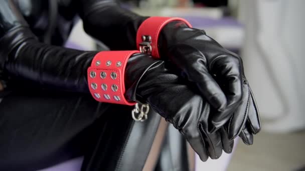 Woman in black outfit with red cuffs close-up. Female hands in leather gloves and handcuffs. - Footage, Video