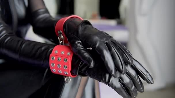 Handen in handschoenen zwart leer en rode manchetten ongericht close-up. Vrouwelijke handen in handboeien defocus. - Video