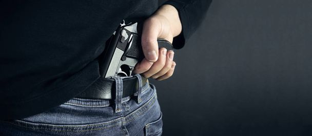 Τρομοκρατικές κλέφτης άνδρας κρατώντας όπλο στο χέρι του. Κρυφό όπλο. Απομονωμένη σε σκούρο φόντο. χώρο αντίγραφο - Φωτογραφία, εικόνα