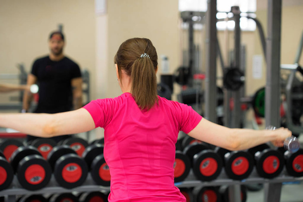 Atrás mujer joven entrena deltoides en el gimnasio
 - Foto, imagen