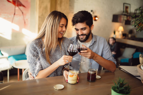 Пара клінкерних окулярів з червоним вином на сьогоднішній день в повсякденному вбранні в кафе. Пара має романтичні моменти
. - Фото, зображення