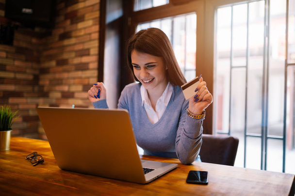 Kredi kartı tutan ve dizüstü bilgisayar kullanan genç bir kadın. Çevrimiçi alışveriş kavramı - Fotoğraf, Görsel