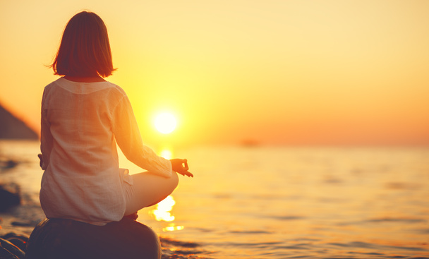 Frau praktiziert Yoga und meditiert in Lotusposition bei Sonnenuntergang - Foto, Bild
