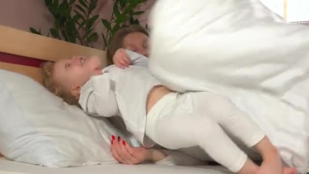 Zlobivý smějící se dívka lehnout si u její matky v posteli - Záběry, video