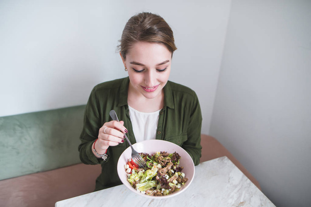 Retrato de uma jovem mulher positiva com uma placa de salada em suas mãos em um interior brilhante. Alimentação saudável
 - Foto, Imagem