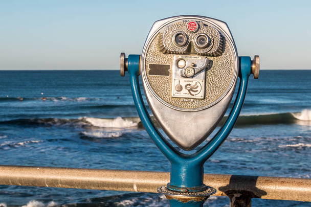 La luz de la mañana brilla en los prismáticos operados con monedas en un muelle de pesca con una vista de las olas del océano en la distancia
.  - Foto, imagen
