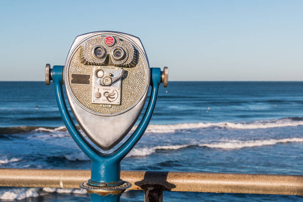Coin-operated binoculars on a fishing pier with a view of ocean waves in the distance.  - Photo, Image