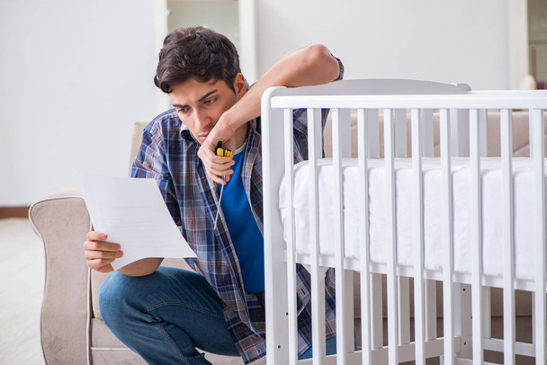 Hombre joven montando cama de bebé con manual de instrucciones - Foto, Imagen