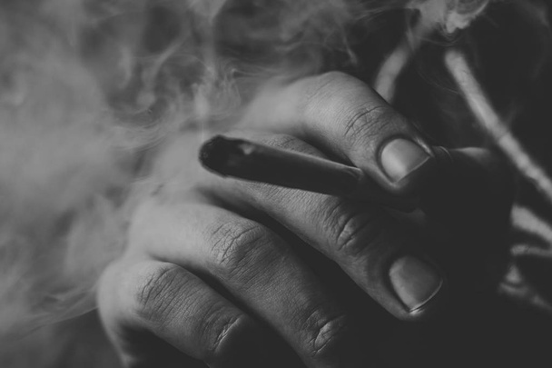Muž kouří konopí plevel, společné a zapalovač ve svých rukou. Kouř na černém pozadí. Koncepce užívání lékařské marihuany a legalizace konopí. Černá a bílá - Fotografie, Obrázek