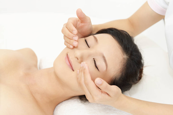 mooie jonge vrouw gezicht massage met gesloten ogen ontvangen in een spa salon  - Foto, afbeelding