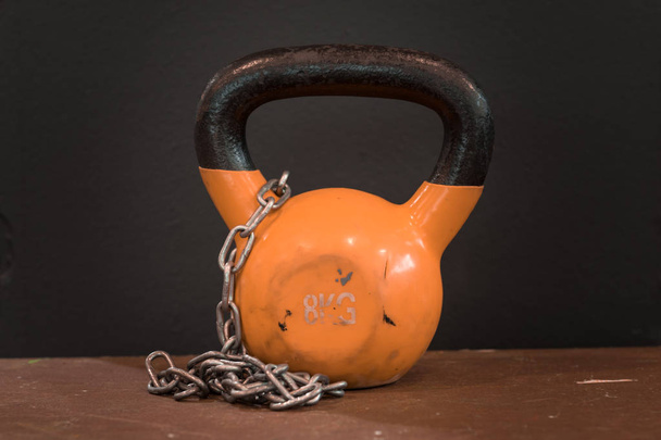 Small orange eight kilograms heavy worn out kettlebell with silver chain against black background. Gym and fitness equipment - Photo, Image