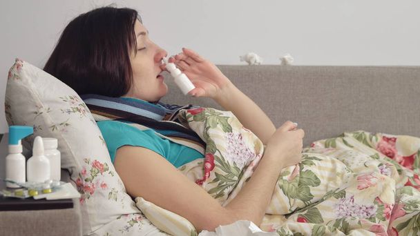 Mujer enferma acostada en la cama en casa, con spray en la nariz
 - Foto, imagen
