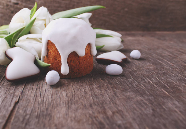 Osterkomposition mit frischen weißen Tulpen, Osterkuchen und glasierten Plätzchen geformte Kaninchen auf Holzgrund - Foto, Bild