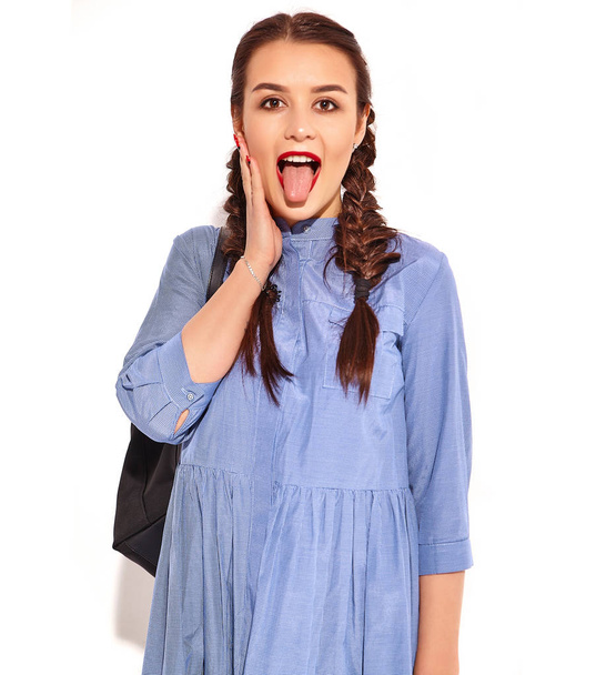 Portrait of young happy smiling woman model with bright makeup and red lips with two horns in hands in summer colorful blue dress and back pack isolated on white. Showing her tongue - Fotoğraf, Görsel