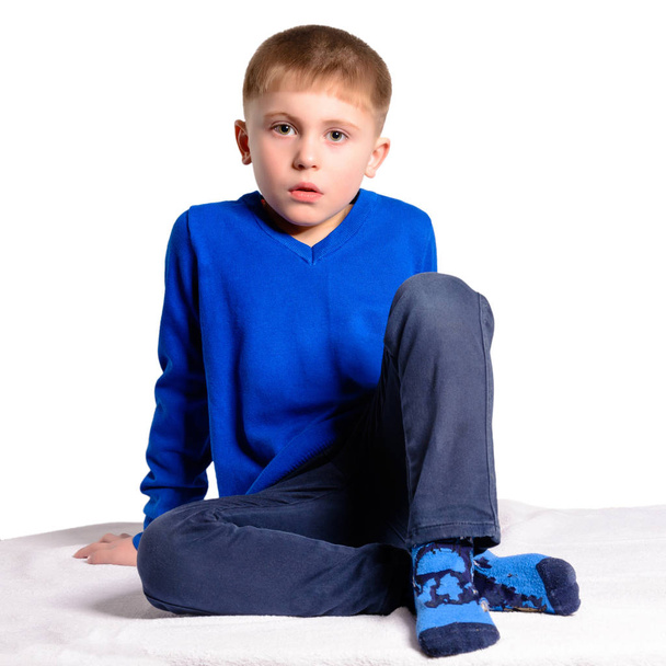 Ένα αγόρι σε ένα μπλε σακάκι κάθεται, απομονώνονται σε λευκό φόντο - Φωτογραφία, εικόνα