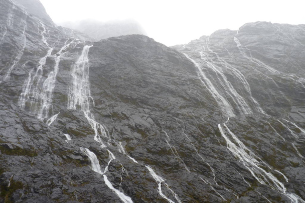 Setki wodospady spływające z gór podczas ulewy w Fiordland National Park, Nowa Zelandia - Zdjęcie, obraz