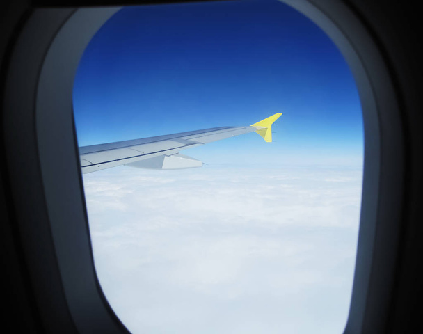 Het gele einde van het vliegtuig is bekeken vanuit een venster boven de witte wolken in een blauwe horizon ergens boven Europa - Foto, afbeelding
