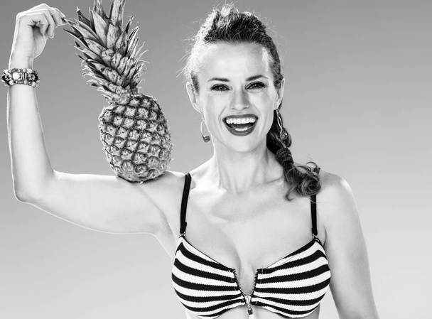 Perfect summer. happy fit woman in swimwear on the seacoast showing pineapple biceps - Foto, Imagen