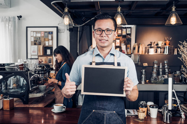 Asian male barista wear jean apron thumbs up at blank blackboard - Фото, зображення