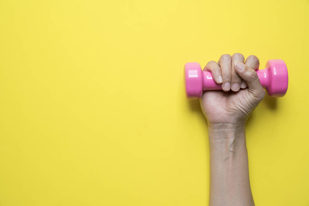 woman hand holding pink dumbbell on yellow background, sport and - Foto, Imagem
