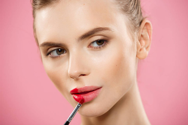 美容コンセプト - ピンクのスタジオの背景に赤い口紅を適用する女性。美しい少女は、メイクアップ. - 写真・画像