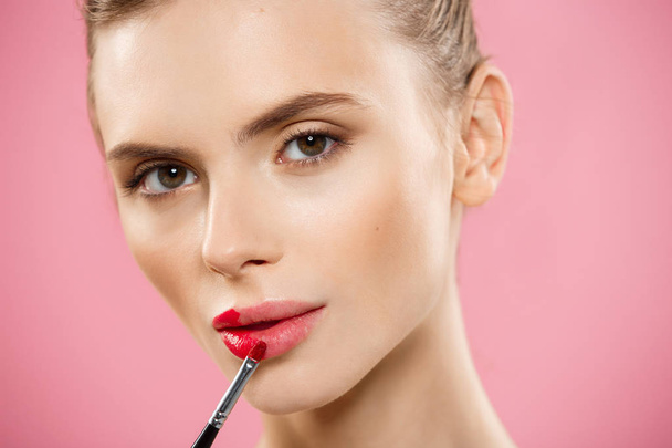 Beauty Concept - Mulher aplicando batom vermelho com fundo de estúdio rosa. Menina bonita faz maquiagem
. - Foto, Imagem