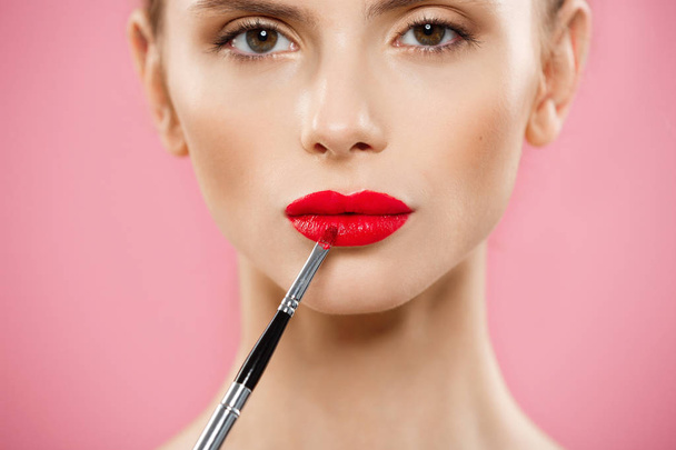 Beauty Concept - Mujer que aplica lápiz labial rojo con fondo de estudio rosa. Hermosa chica hace maquillaje
. - Foto, Imagen