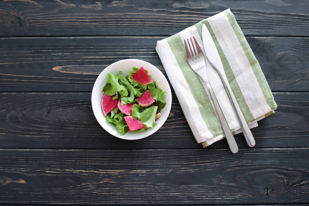 Salada com rábano de melancia (daikon chinês) e alface em uma placa branca em um fundo de madeira
 - Foto, Imagem