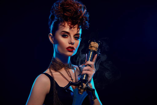 Glamorous woman with fashionable hairdress keeping steel sword. - Foto, afbeelding