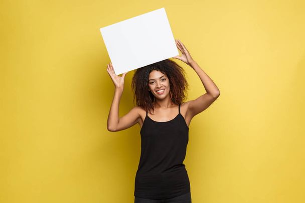 Business Concept - Close up Portrait young beautiful attractive African American smiling showing plain white blank sign. Yellow Pastel studio Background. Copy space - Photo, Image