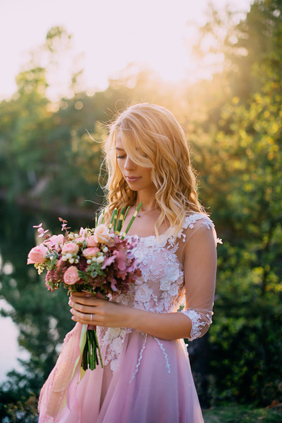 beautiful bride stands with a bouquet in hands on a nature background - Фото, зображення