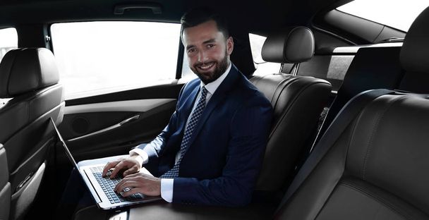 smiling businessman sitting in the back seat of a prestigious car - Фото, изображение