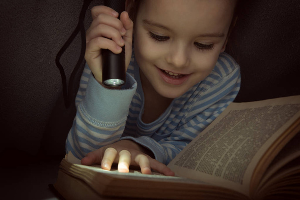 Pieni tyttö lukee satuja kirjan peiton alla aattona
 - Valokuva, kuva